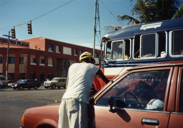 El señor que limpia vidrios, tan común en los semáforos. En la foto se observa también un autobús de los llamados "Banderitas" que ya desaparecieron.