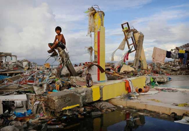 TACLOBAN, PHILIPPINES - NOVEMBER 13: A young boy sits on the ruins of a building amid scenes of devastation in the aftermath of Typhoon Haiyan on November 13, 2013 in Tacloban, Leyte, Philippines. Typhoon Haiyan, packing maximum sustained winds of 195 mph (315 kph), slammed into the southern Philippines and left a trail of destruction in multiple provinces, forcing hundreds of thousands to evacuate and making travel by air and land to hard-hit provinces difficult. Around 10,000 people are feared dead in the strongest typhoon to hit the Philippines this year. (Photo by Kevin Frayer/Getty Images)