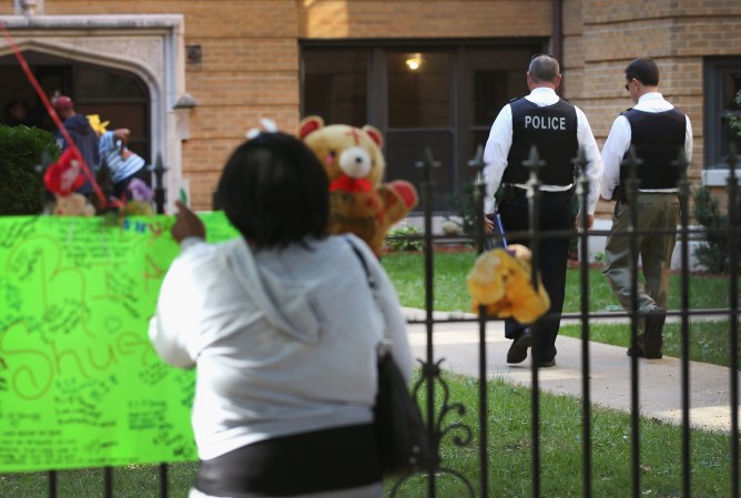 CHICAGO, IL - OCTOBER 10: A woman signs a makeshift memorial to three men who were shot and killed yesterday as police comb the South Shore neighborhood for clues to the crime on October 10, 2013 in Chicago, Illinois. Sylvester Solomon, 27, Darrius Morris, 23, and Rasheed Trull, 16, were killed when a gunman opened fire from a car while they were standing in front of an apartment complex. Trull's twin brother Raheem, who was also at the scene, escaped without injuries after taking cover behind parked cars. (Photo by Scott Olson/Getty Images)