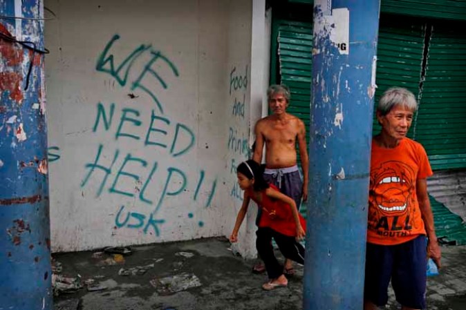 TACLOBAN, PHILIPPINES - NOVEMBER 13: Residents stand next to grafitti requesting aid in the aftermath of Typhoon Haiyan on November 13, 2013 in Tacloban, Leyte, Philippines. Typhoon Haiyan, packing maximum sustained winds of 195 mph (315 kph), slammed into the southern Philippines and left a trail of destruction in multiple provinces, forcing hundreds of thousands to evacuate and making travel by air and land to hard-hit provinces difficult. Around 10,000 people are feared dead in the strongest typhoon to hit the Philippines this year. (Photo by Kevin Frayer/Getty Images)