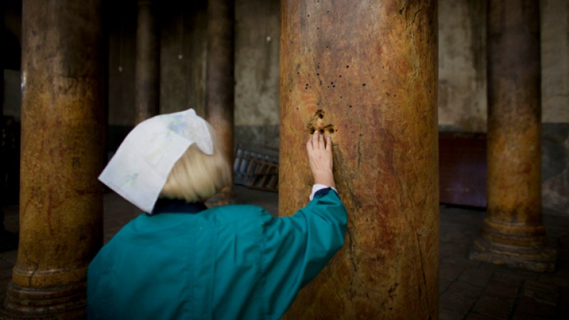 Una mujer coloca sus dedos en unos agujeros en forma de cruz en las antiguas columnas de la Iglesia de la Natividad, en Belén, un lugar con mucho significado para los cristianos pues se cree fue aquí donde nació Jesús.