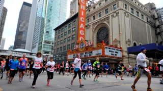 Participantes de la maratón de Chicago corren por la calle State y al fondo el Chicago Theatre.