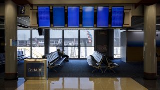 A passenger sits beneath a nearly empty departures board in the American Airlines Group Inc. at O'Hare International Airport (ORD) in Chicago