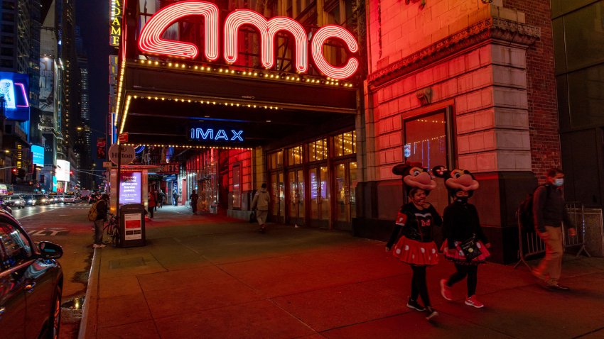 Street performers in Minnie Mouse costumes pass in front of an AMC movie theater at night in the Times Square neighborhood of New York, Oct. 15, 2020.