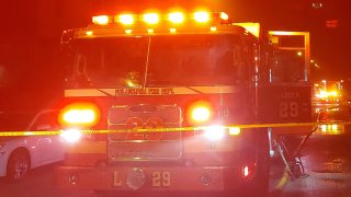 A Philadelphia Fire Department truck has its lights on as it parks behind crime scene tape following a fatal blaze in the West Oak Lane neighborhood.