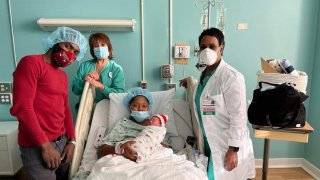 Padres posando con su recien nacido en cuarto de hospital junto a enfermera y doctora.