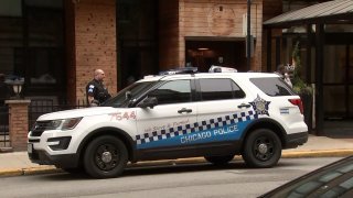 A standard Chicago police SUV, primarily white with blue and black striping, sits outside of a red-brick business in Gold Coast after a person was found shot to death at the scene