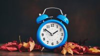 Vibrant blue clock with real fall leaves to portray daylight savings time and clocks falling back an hour