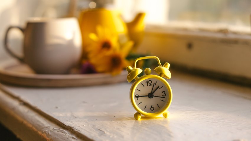 Fall seasonal still life. Retro alarm clock. Fall back concept. Cup with autumn flowers and kettle on wooden tray on window sill