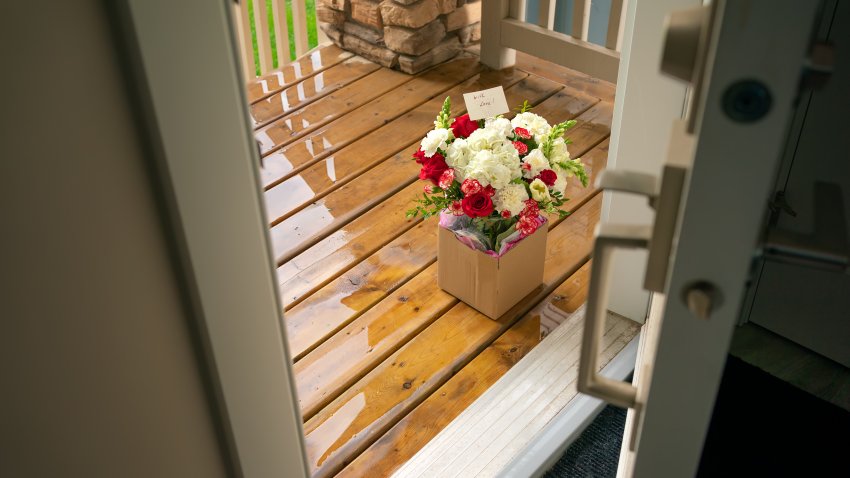 A bouquet of flowers in a carton box on a porch of a house through open door. Surprise contactless delivery of flowers for woman. Delivery of goods home during quarantine. A pleasant unexpected gift.