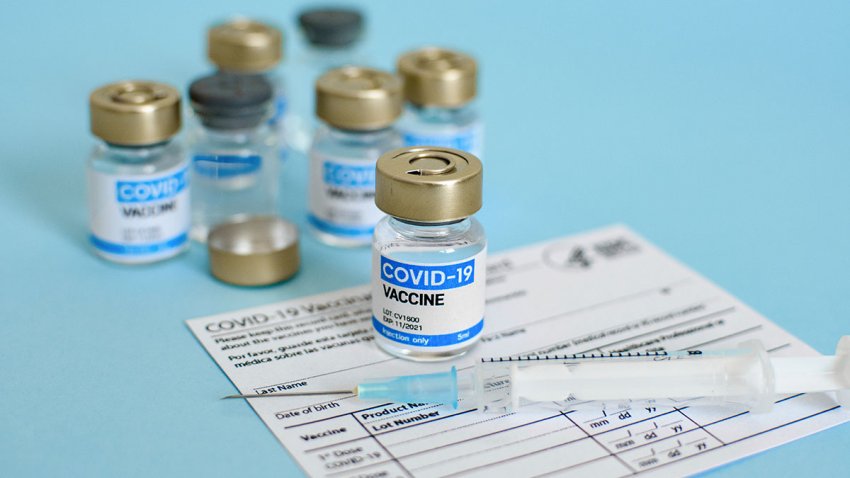 Covid-19 vaccine vial and syringe on CDC vaccination record card on blue background.