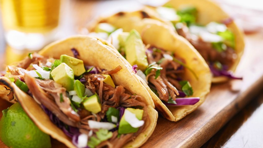 three  pork carnitas street tacos in yellow corn tortilla with avocado, onion, cilantro and cabbage