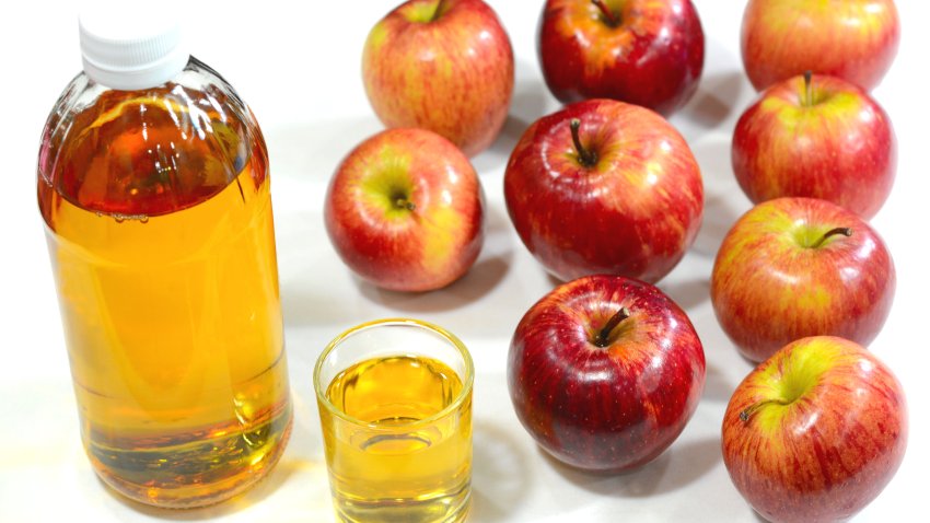 Apple cider vinegar in a cup and bottle with red apples on the background.