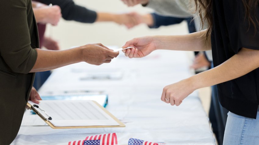 Unrecognizable polling place volunteer receives an id card from a female voter.