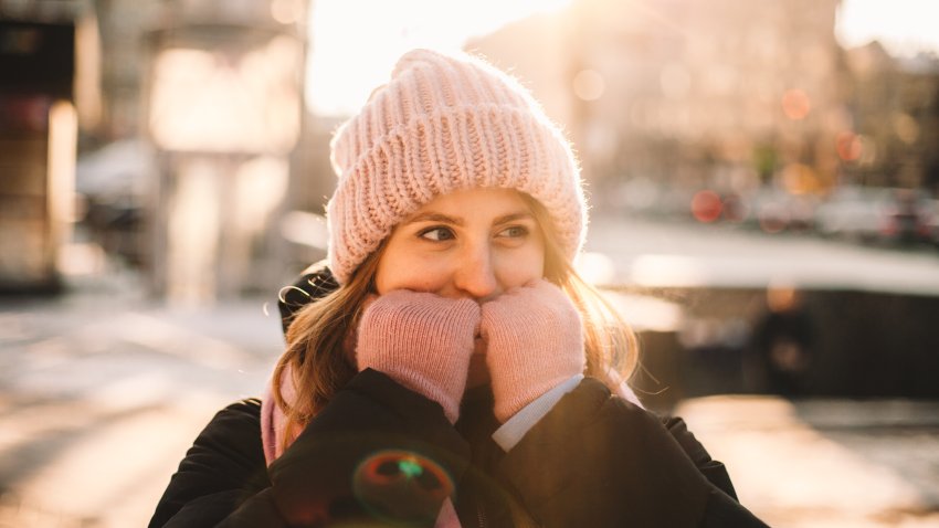 Young woman warming her hands while standing on the street in city during cold weather in winter