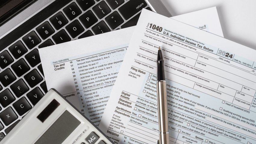 A close-up of a 1040 U.S. Individual Income Tax Return form, placed on a laptop keyboard with a pen and calculator.