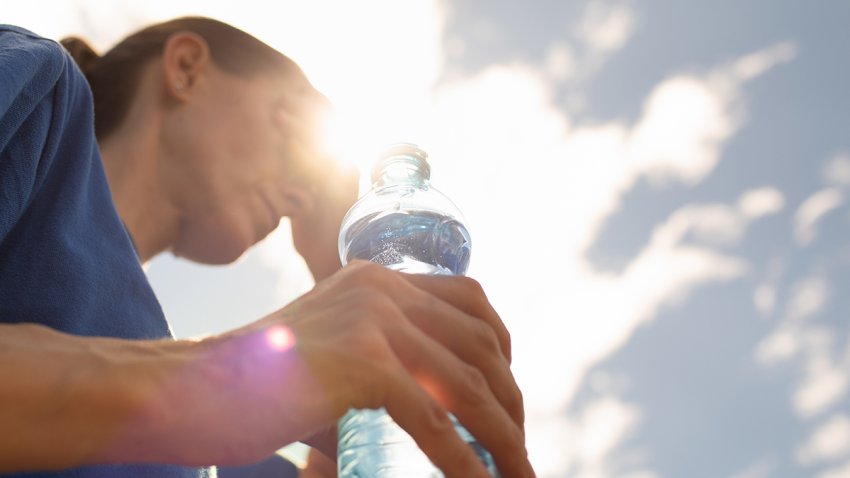 woman drinking water cooling off in extreme summer heat wave, person drinks from water bottle replenish fluids
