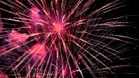 Fireworks bursting brightly in the night sky, creating a festive display of red and pink light for a celebration