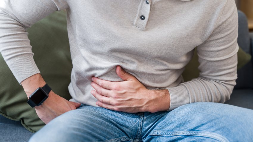 Man struggling with stomach ache, clutching abdomen in pain on sofa at home