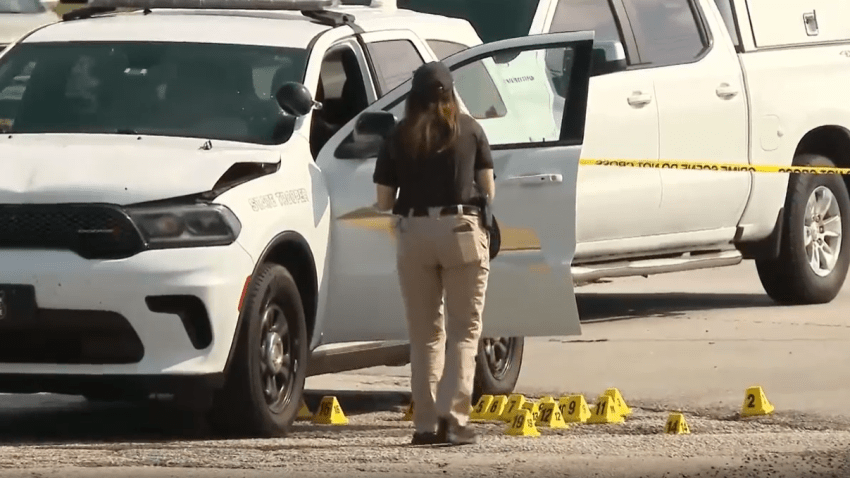 Una oficial tomando fotos de una patrulla de la policía estatal de Indiana y los marcadores de bala en el suelo.