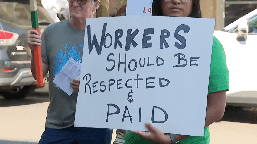 Una persona sujetando una pancarta que dice en inglés Workers should be respected and paid