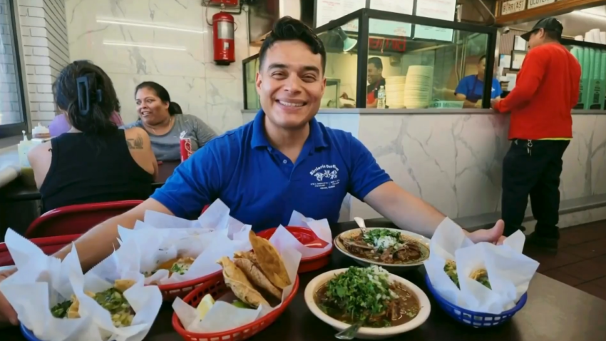 Un hombre sentado en una mesa mostrando platillos de birria.